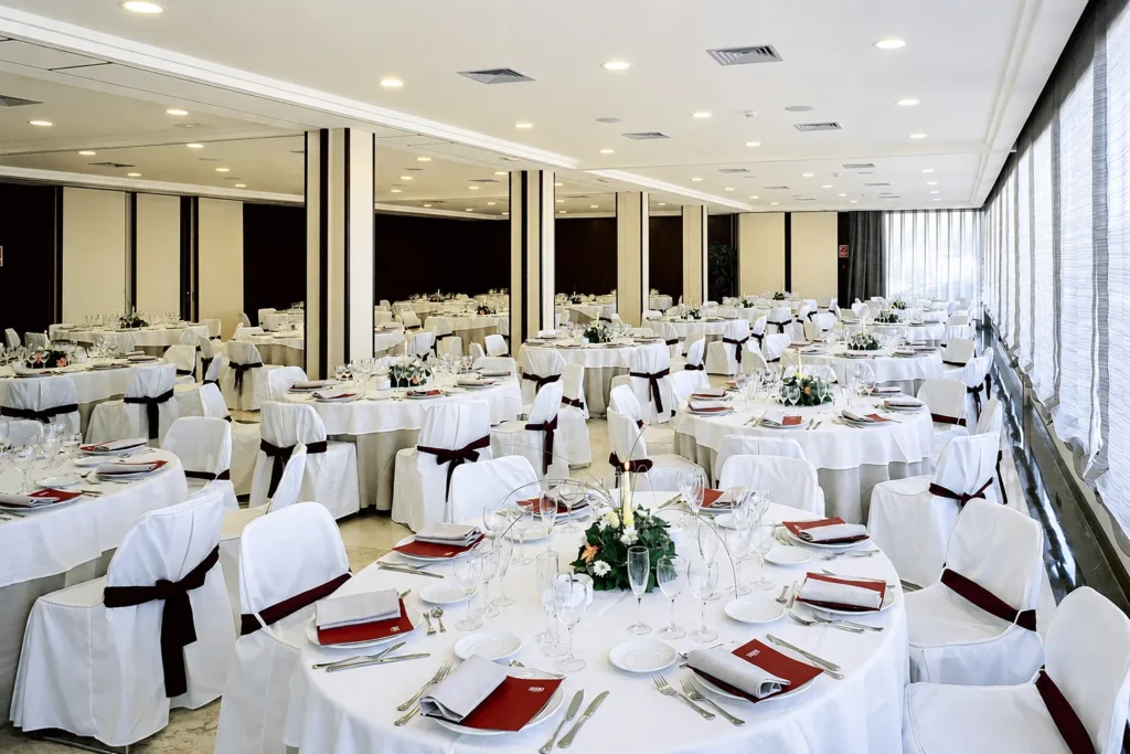 Comedor de hotel con mesas servidas, copas y manteles blancos, luces empotradas