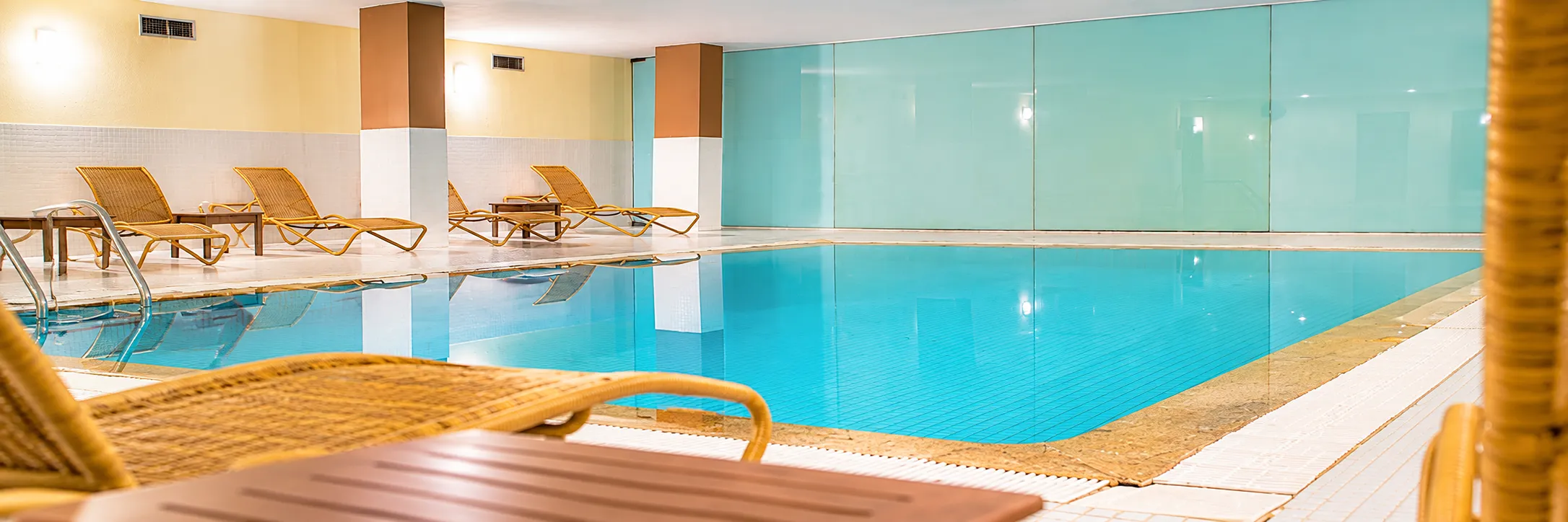 Piscina cubierta con tumbonas y paredes de vidrio color azul turquesa