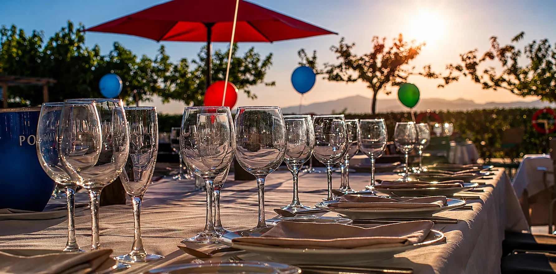Mesa exterior con copas de vino y paraguas rojos al atardecer