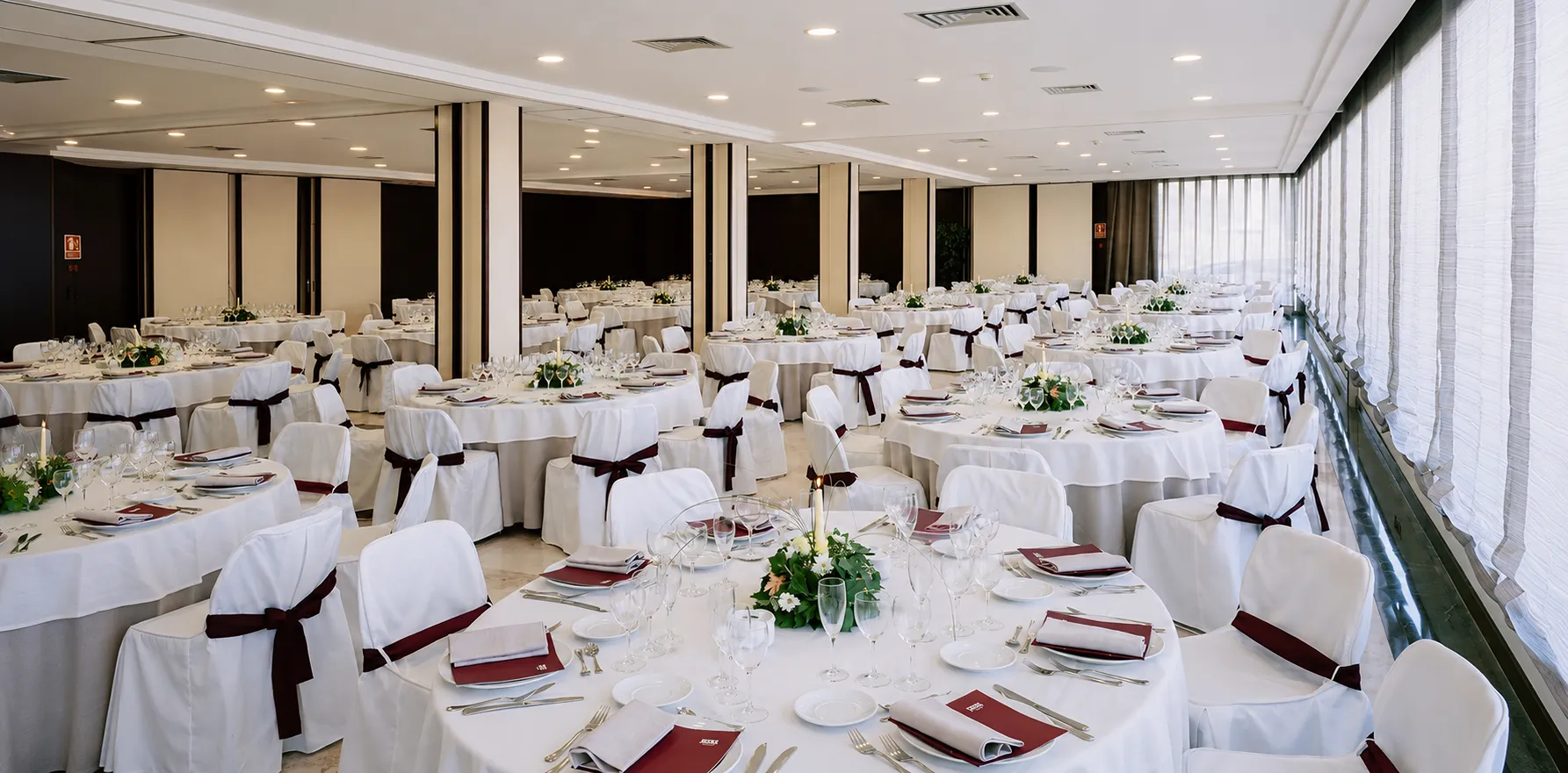 Sal&oacute;n de banquete con mesas servidas, manteles blancos y decoraciones verdes