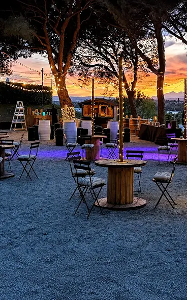 Patio con sillas y luces decorativas, &aacute;rboles y atardecer al fondo.