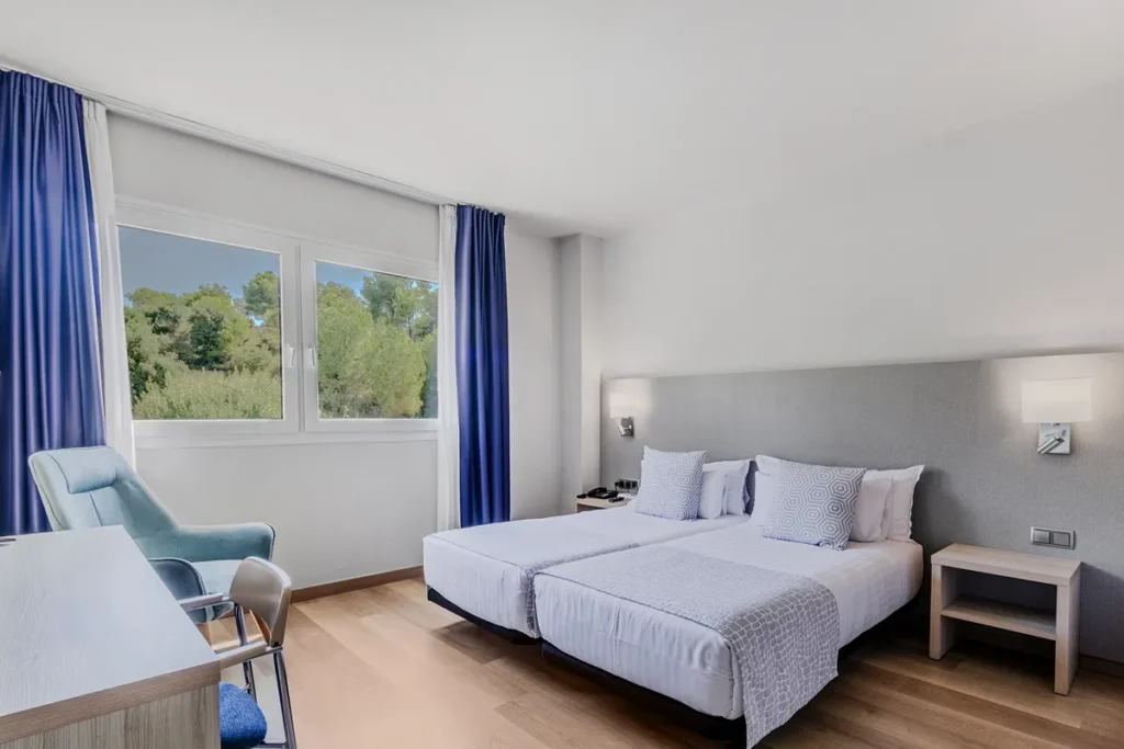 Dormitorio moderno con cama doble, sill&oacute;n y cortinas azules, junto a ventana