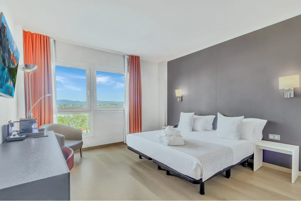 Dormitorio moderno con cama doble, sill&oacute;n y cortinas naranjas junto a ventana