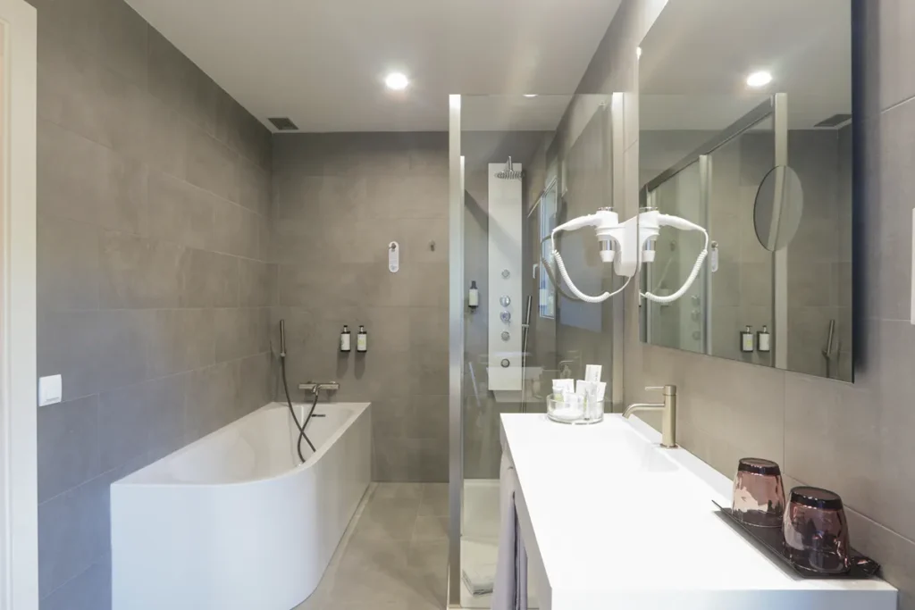 Ba&ntilde;o moderno con ba&ntilde;era blanca, lavabo doble, ducha y espejo iluminado