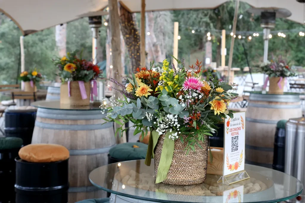 Arreglo floral multicolor en jarr&oacute;n de malla dorada sobre mesa de evento al aire libre