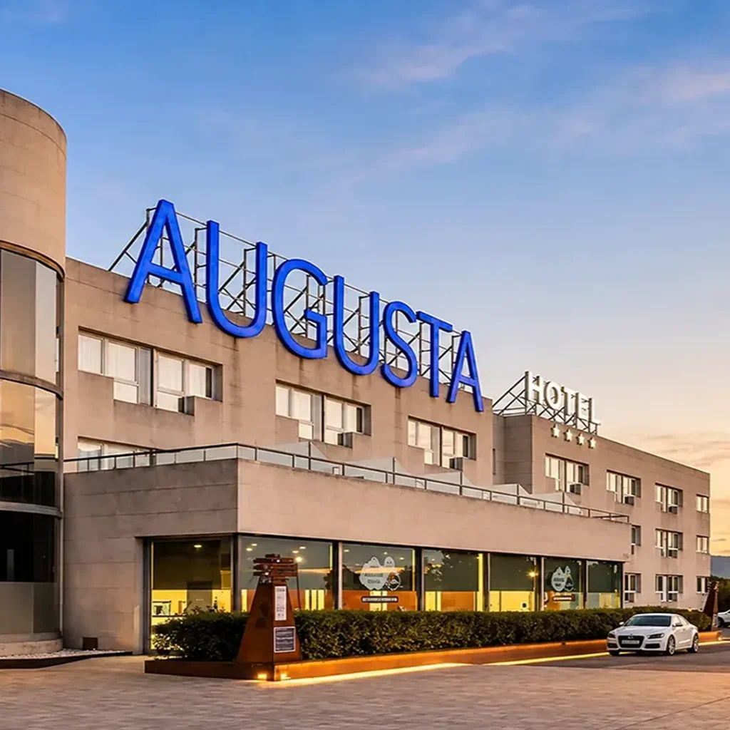 Fachada del hotel BlauClAsista con letrero luminoso azul al atardecer