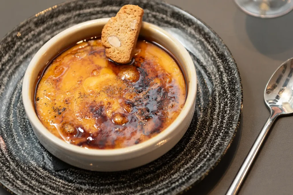 Crema con costra tostada, servida en cuenco sobre plato oscuro.
