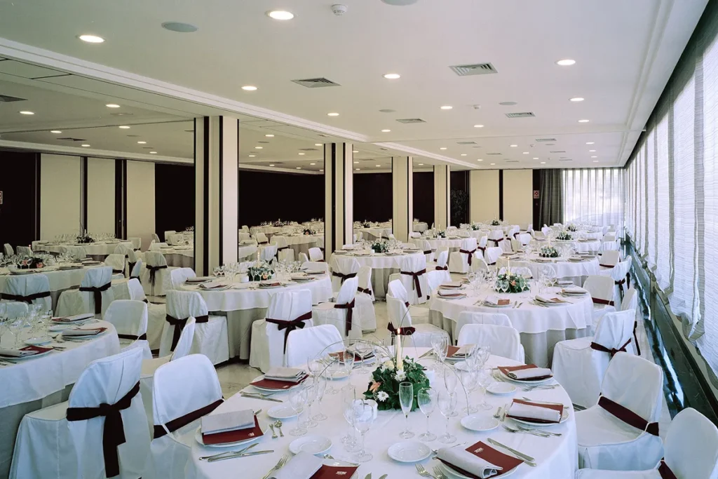 Sal&oacute;n de banquete con mesas servidas y vajilla bajo luces de techo