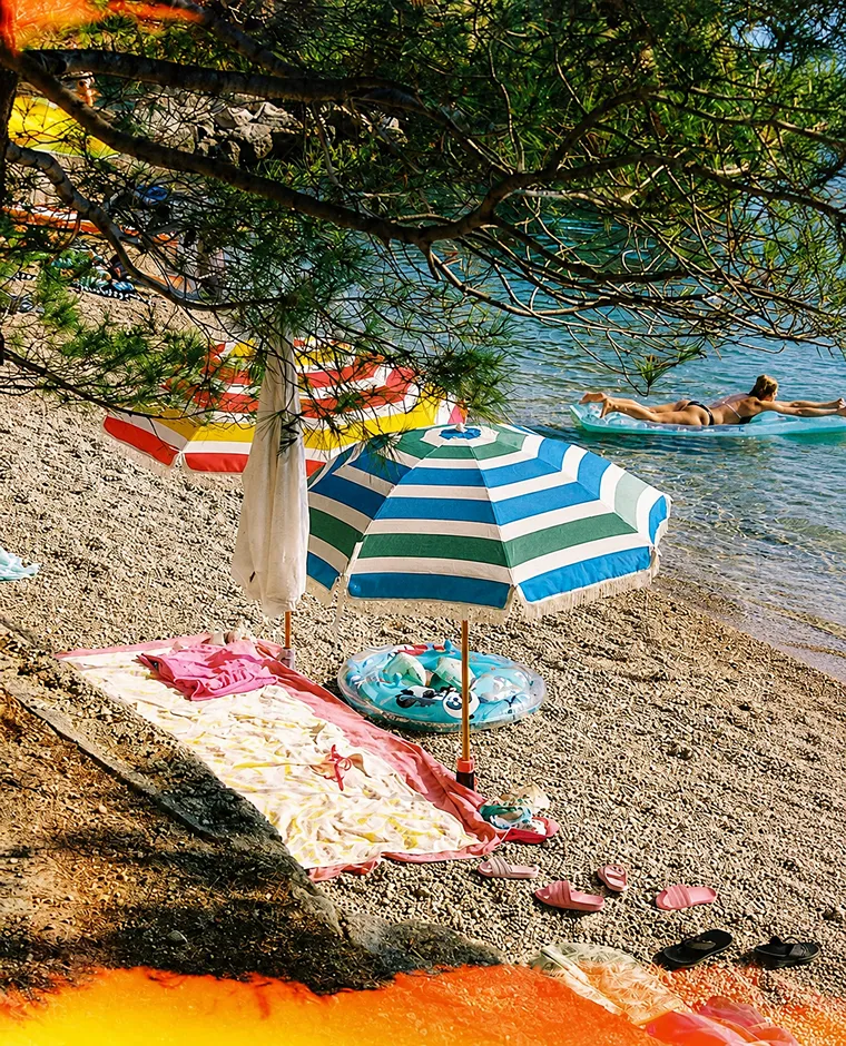 Playa con sombrilla, mantas y una persona nadando en el mar