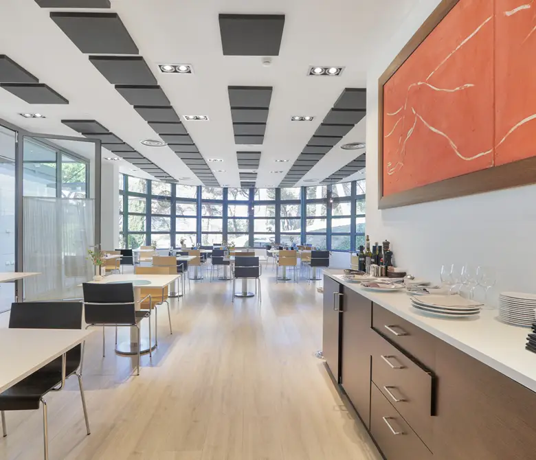 Interior de una oficina luminosa con mesas, sillas y cocina con vajilla.
