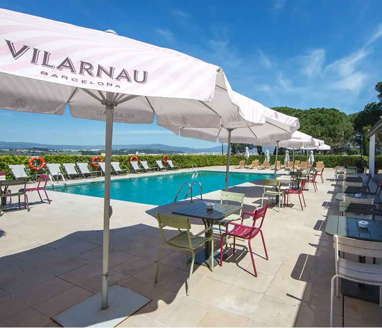 Terraza con piscina, tumbonas y sombrillas Vilarnau en un d&iacute;a soleado.