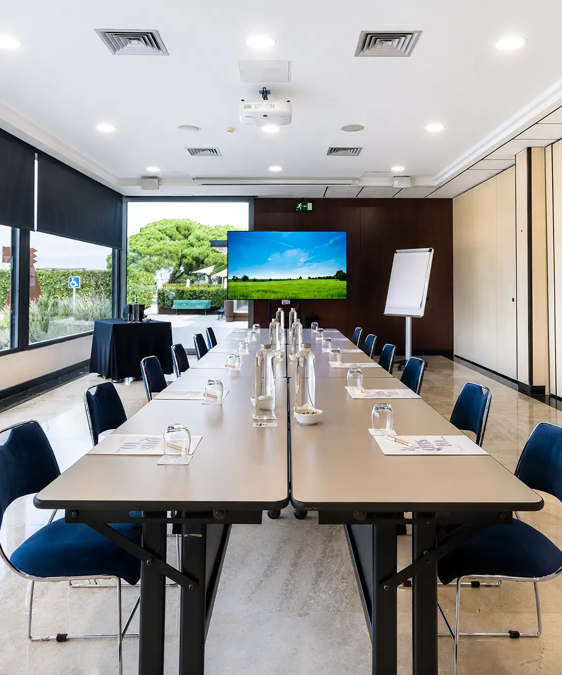 Sala de reuniones moderna con mesa, pantallas y proyector en el techo