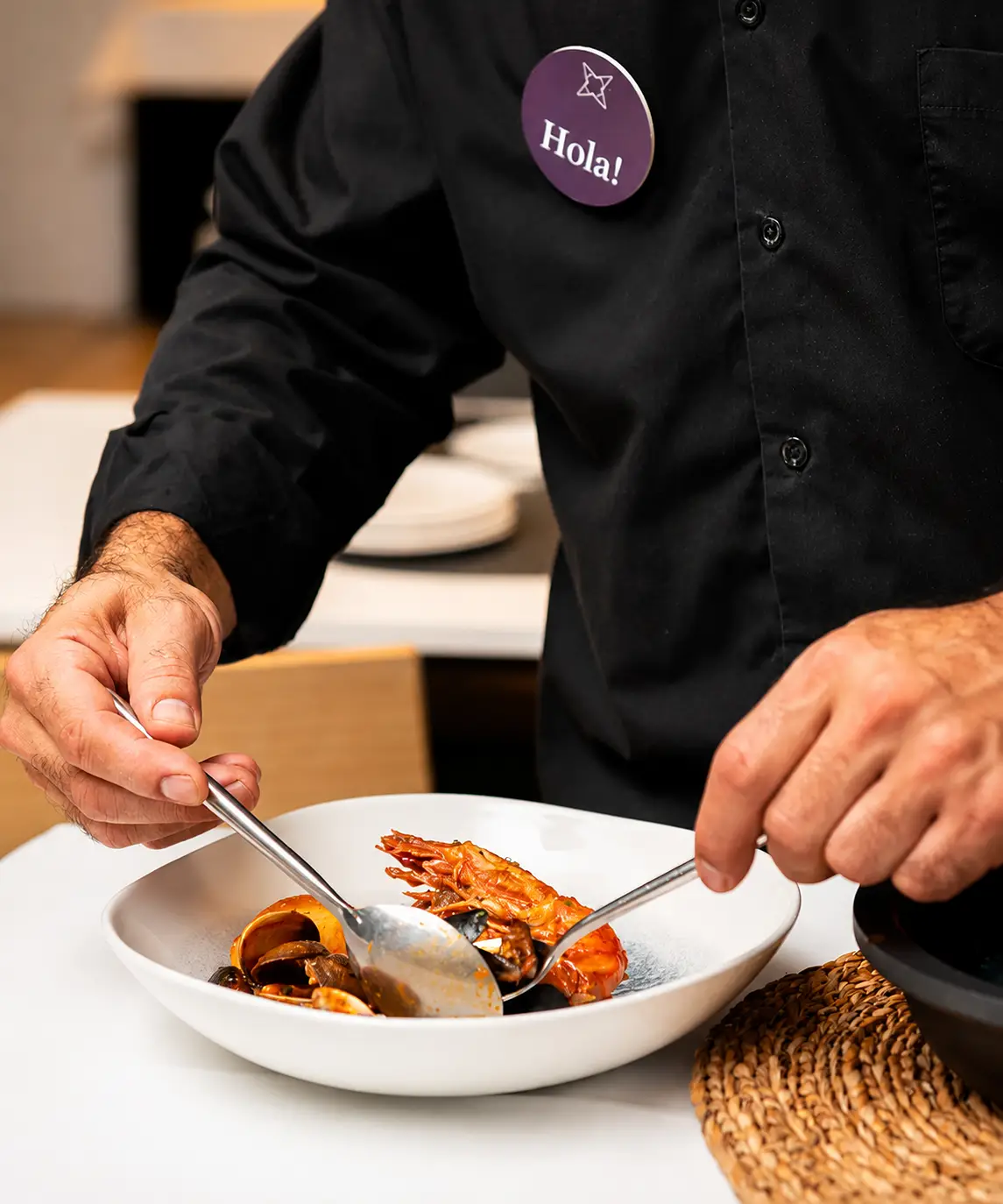 Chef con credencial &ldquo;Hola!&rdquo; sirve comida en un plato blanco
