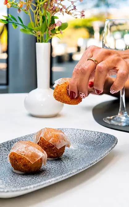 Mano sirve un bocadillo de empanada sobre plato; mesa con flores y copas