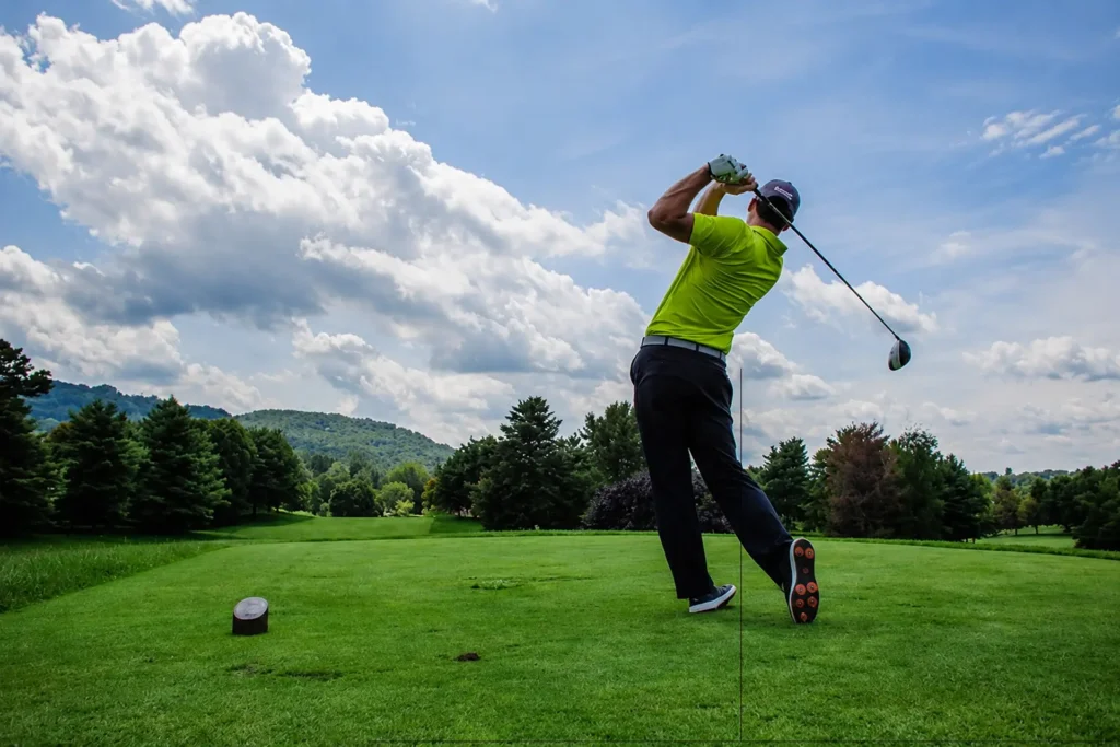 Golfista con camiseta verde golpeando la pelota en un campo, bajo nubes