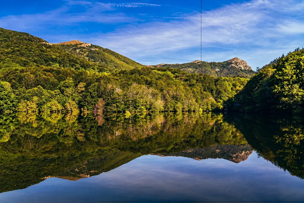 Paisaje de monta&ntilde;as cubiertas de vegetaci&oacute;n con cielo azul reflejado en un lago