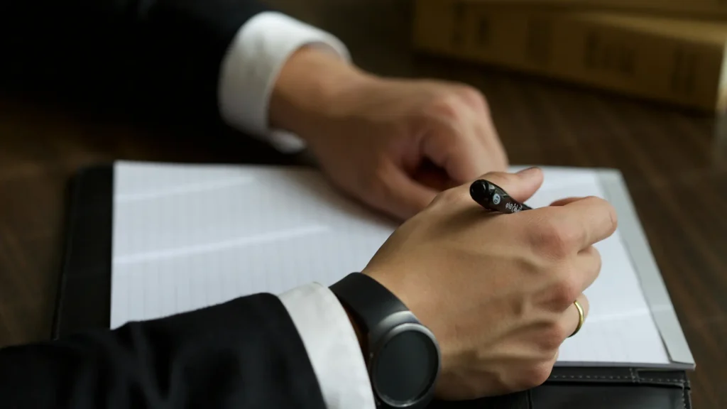 Mano con bol&iacute;grafo sobre cuaderno, una persona escribe en casa