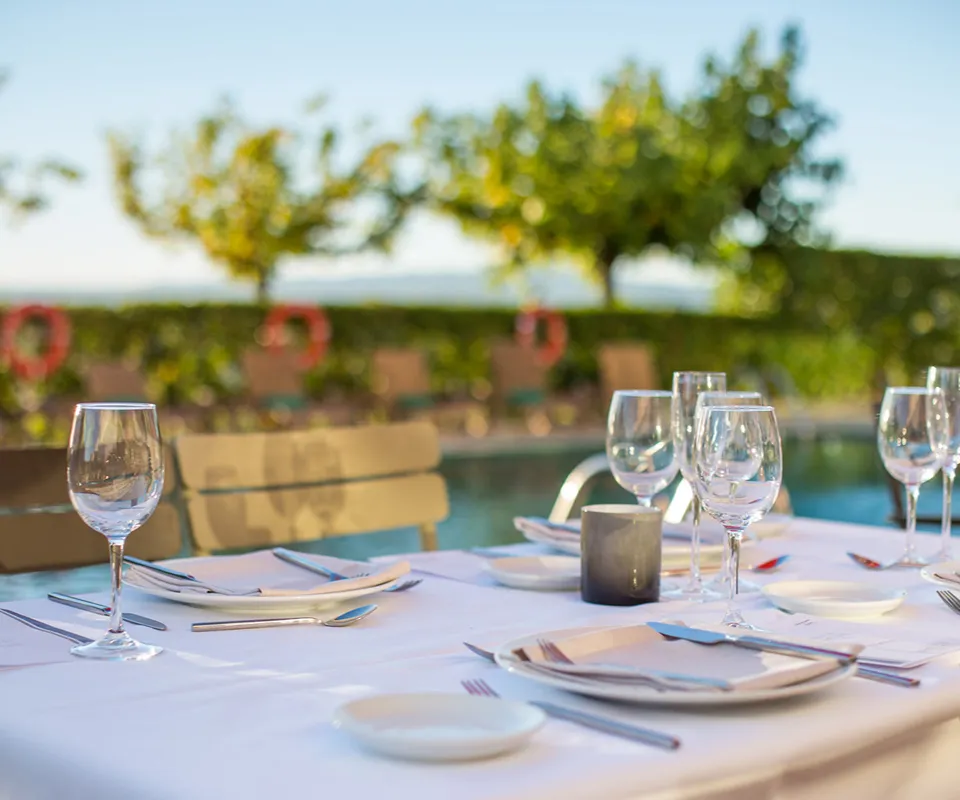 Mesa con copas y cubiertos junto a una piscina, al aire libre.