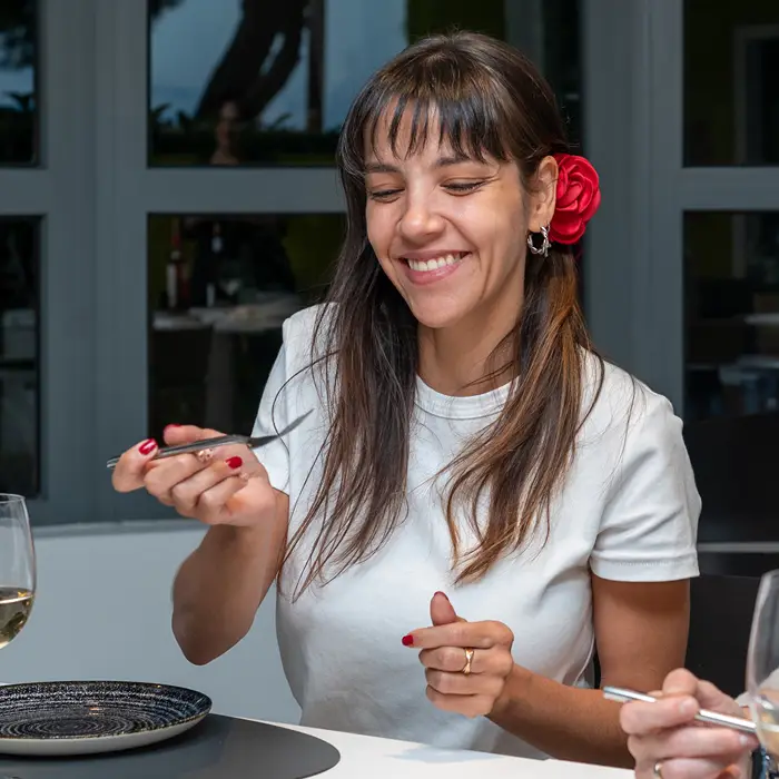 Mujer sonriente con flor roja en el pelo y celular en la mesa