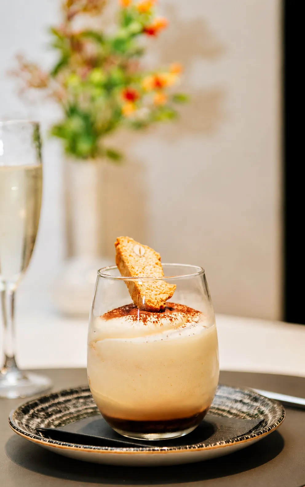 Vaso con bebida cremosa y galleta encima, en bandeja con luz c&aacute;lida.