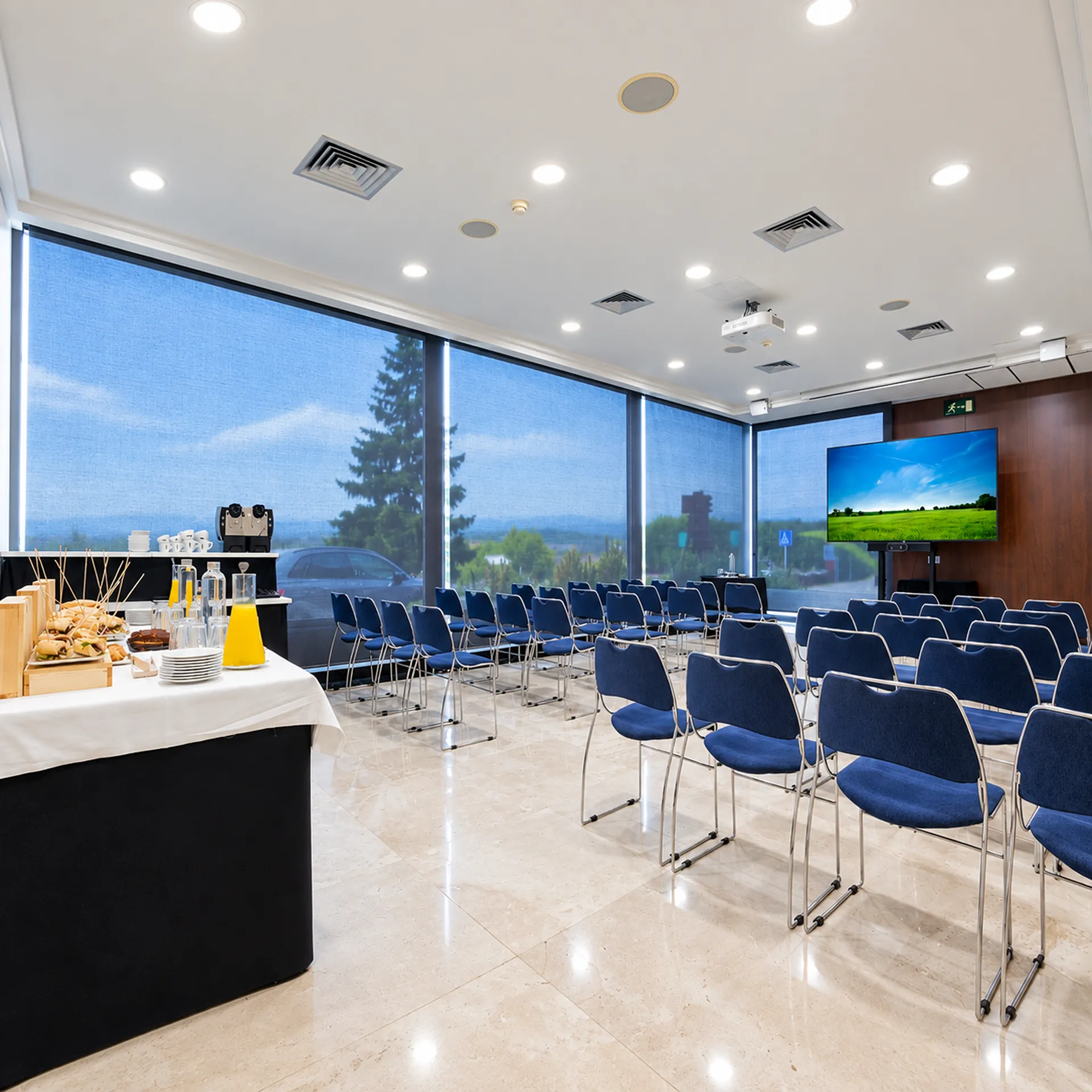 Sala de reuniones con sillas azules, mesas y proyector con luz de techo