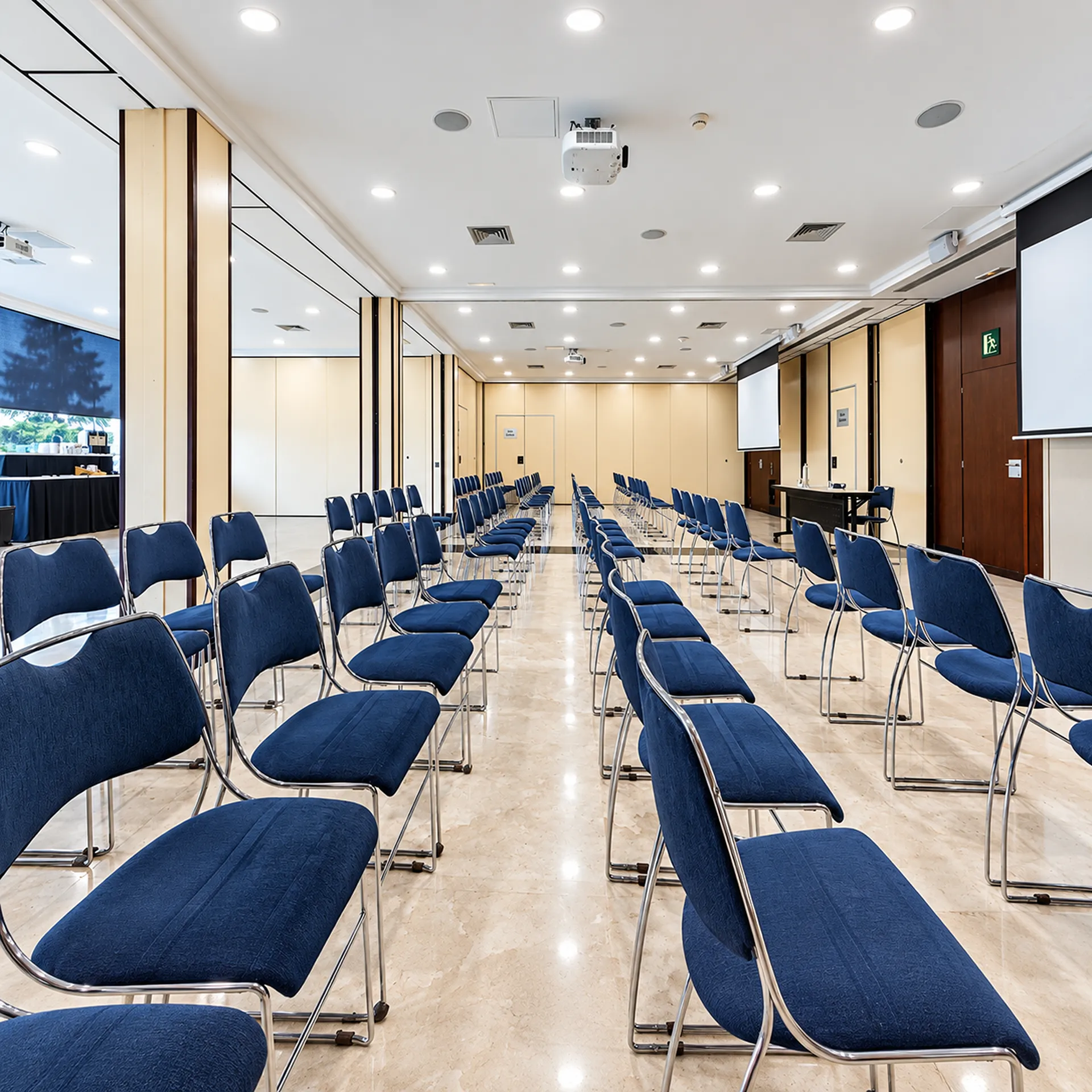 Sala de conferencias con filas de sillas azules y proyector en el techo