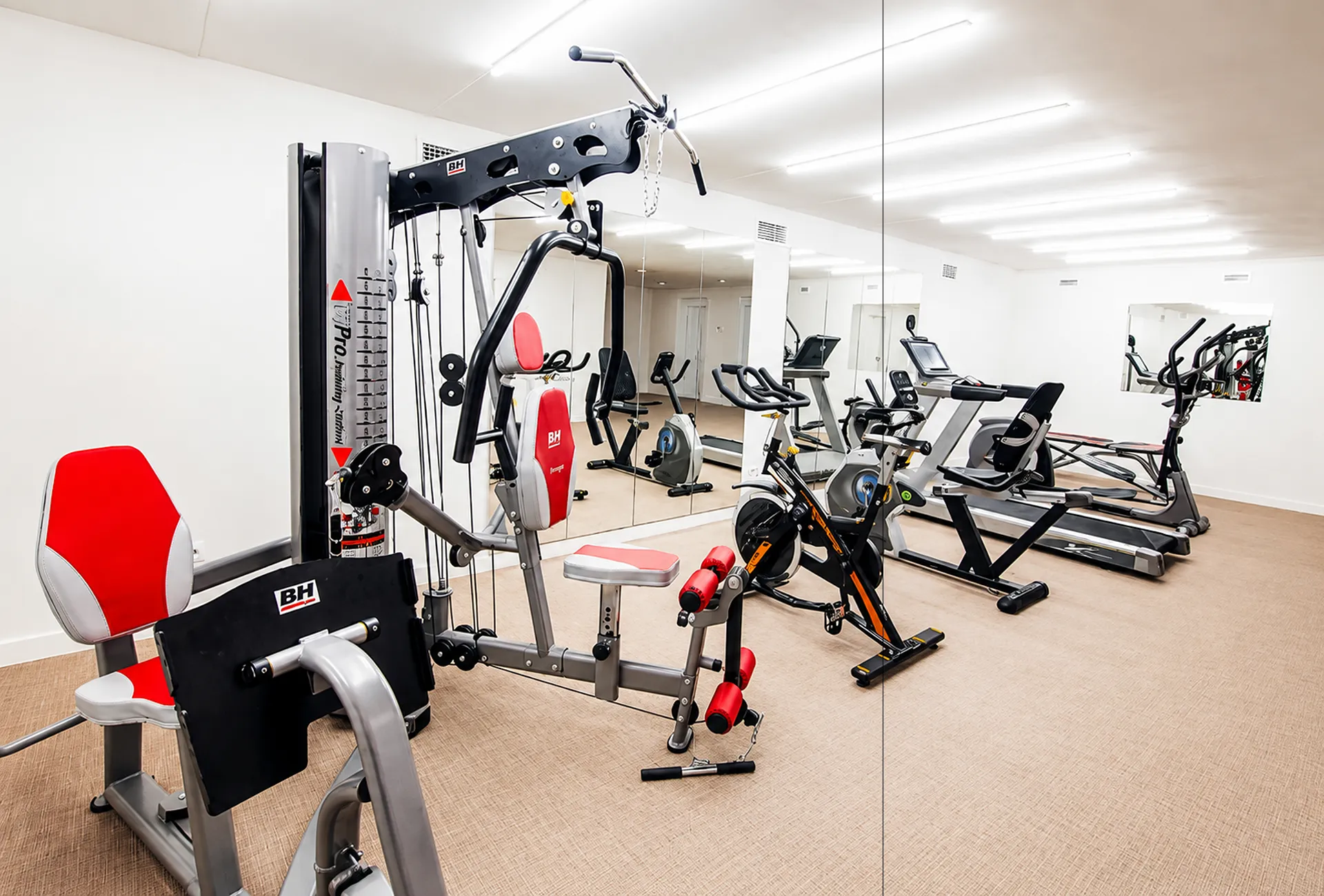 Gimnasio con m&aacute;quinas de ejercicio y bicicletas est&aacute;ticas en sala blanca