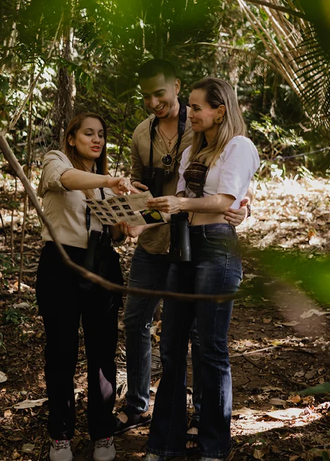 Tres personas en la selva revisando una c&aacute;mara entre plantas tropicales.