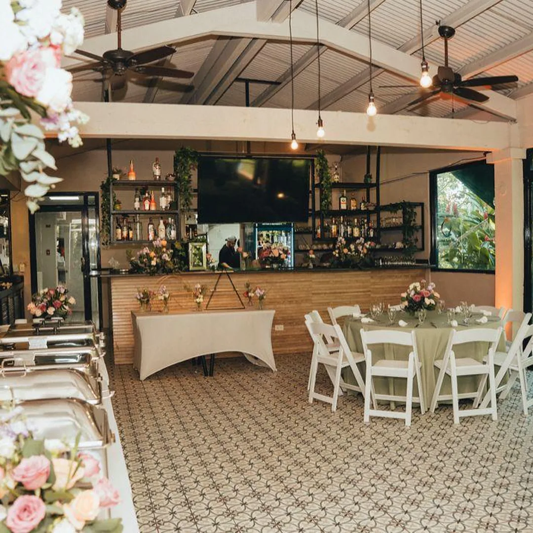 Interior de banquete con barra, luces colgantes y mesas con sillas blancas