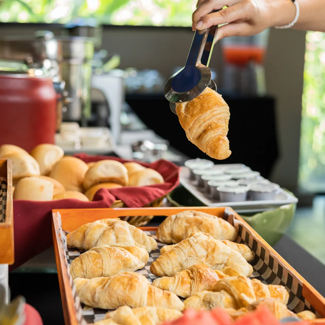 Mano sirve un croissant caliente de una bandeja con pinzas met&aacute;licas
