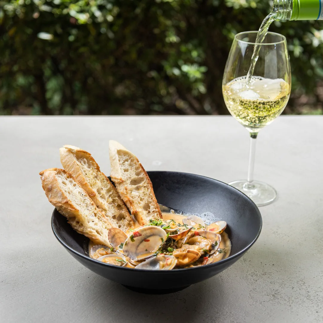 Taz&oacute;n con mariscos en salsa, pan tostado y copa de vino al aire libre