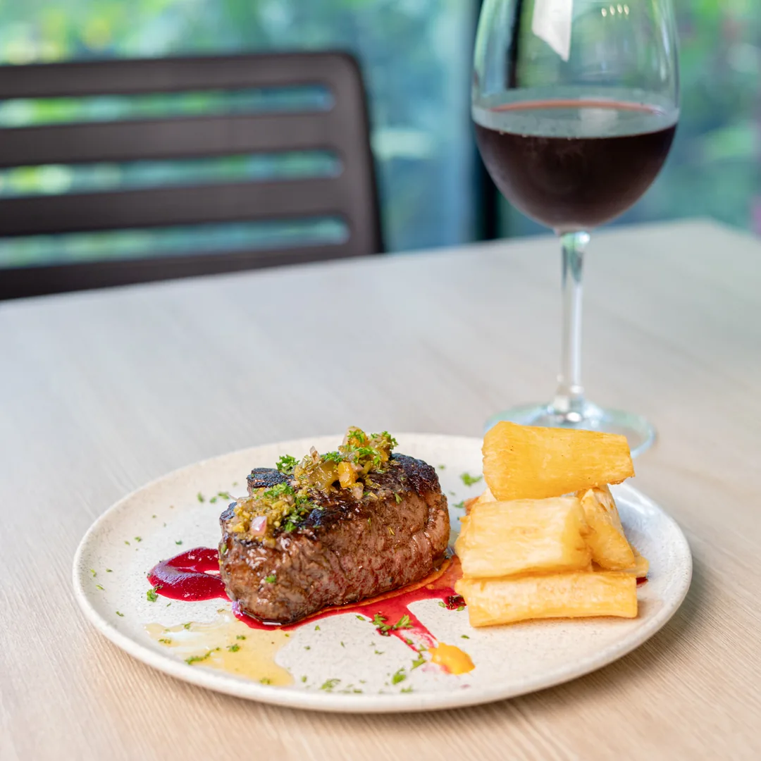 Plato con carne a la parrilla, queso y salsa, con copa de vino detr&aacute;s