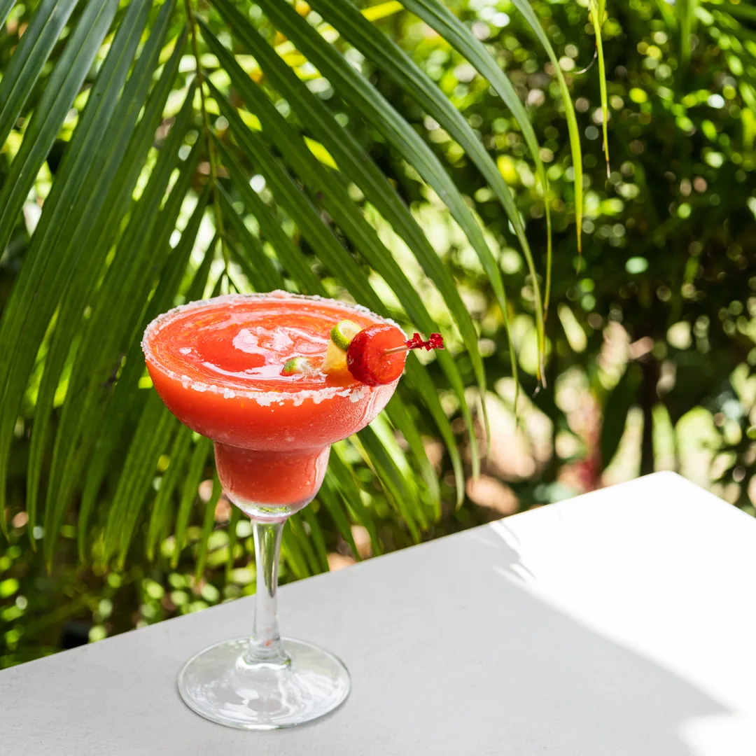 C&oacute;ctel rojo con limonada sobre copa, junto a palmeras en exterior soleado
