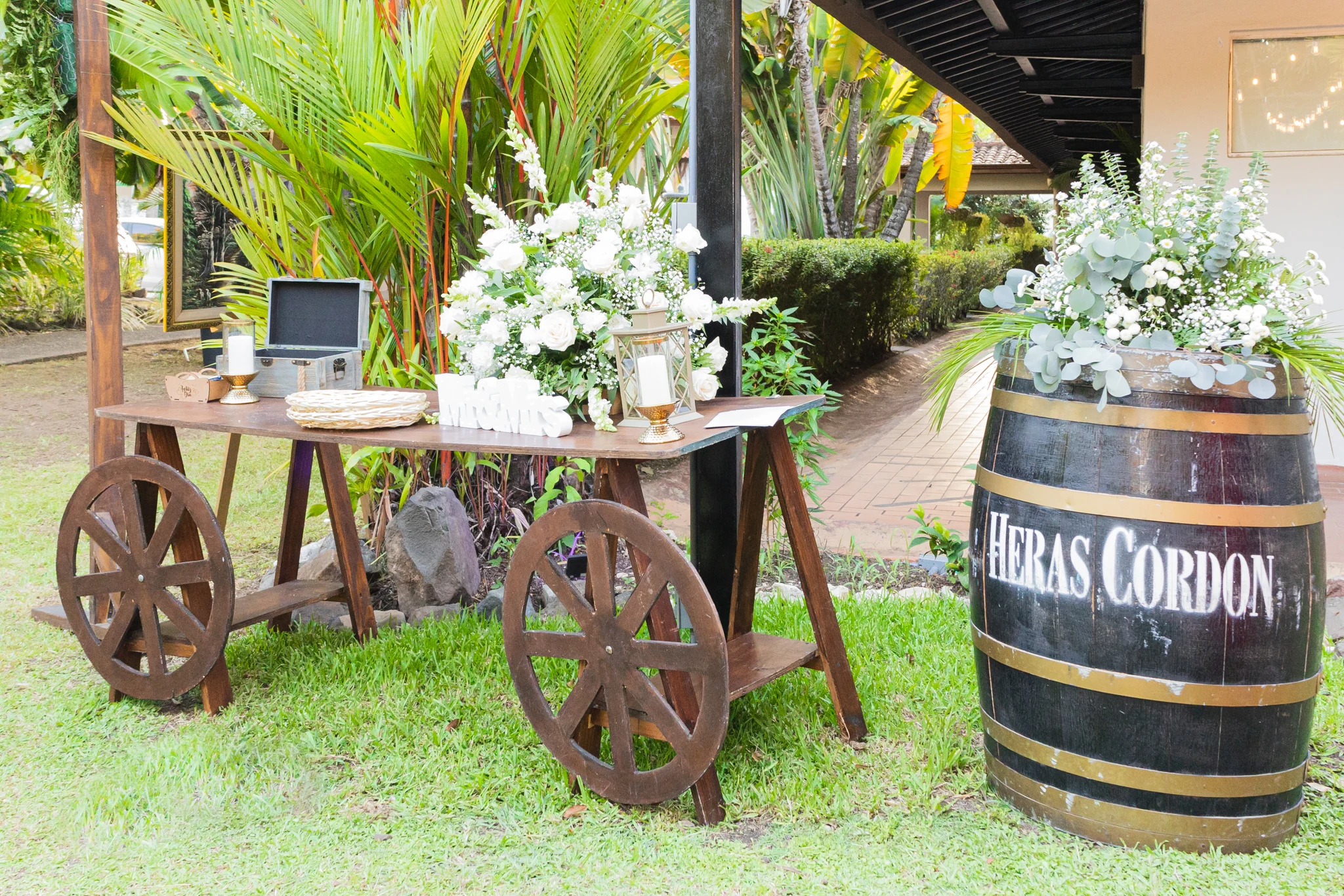 Mesa de banquete con flores blancas, barril decorativo y palmeras al fondo