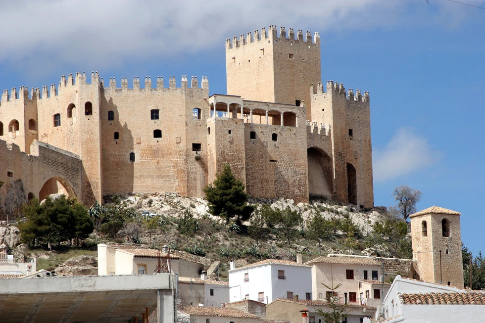 Castillo medieval de piedra sobre un cerro con casas y cielo azul