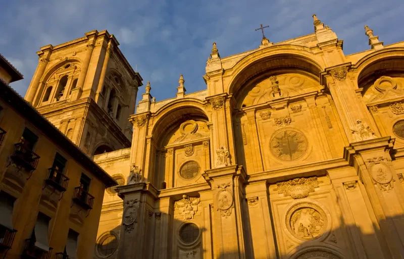 Fachada barroca de catedral de piedra dorada con cielo azul.