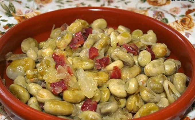 Ensalada de habas con trozos de jamón y verduras en un tazón rojo