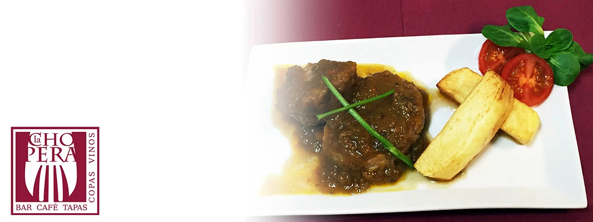 Plato con carne, patatas fritas y tomate con albahaca.
