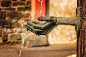 Mano de bronce vierte agua por el borde de una fuente en exterior.