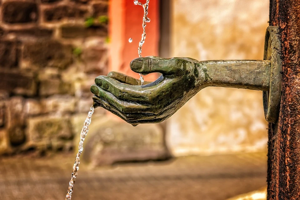 Mano de bronce vierte agua por el borde de una fuente en exterior.