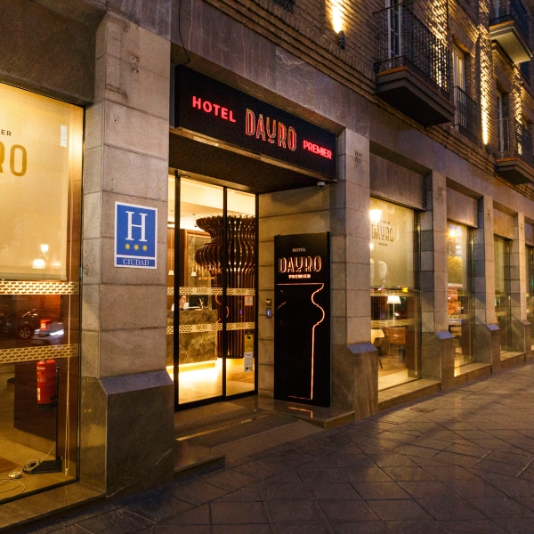Entrada del Hotel D&rsquo;Avilo Premier con puerta iluminada y fachada nocturna