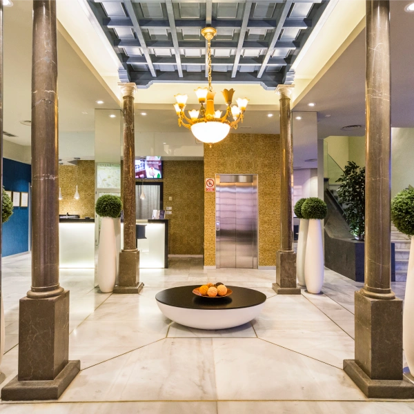Lobby elegante con columnas, candelabro dorado y ascensor al fondo