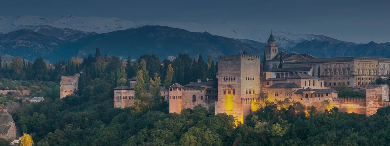 Alhambra iluminada al atardecer con montañas nevadas al fondo