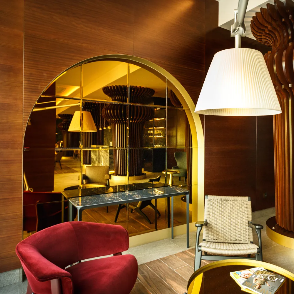 Interior de hotel con mesa, silla roja, espejo y l&aacute;mpara de pie iluminada