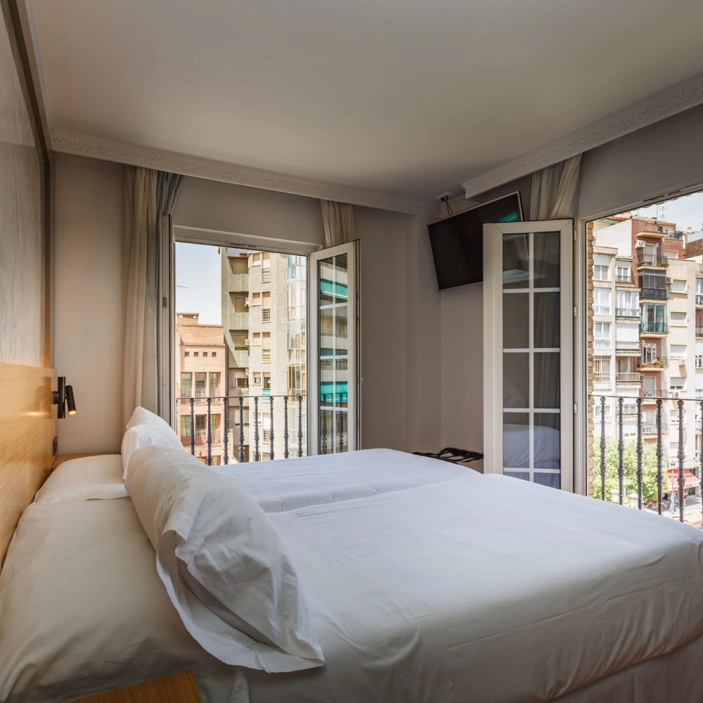 Dormitorio moderno con cama blanca y puertas corredizas al balc&oacute;n.