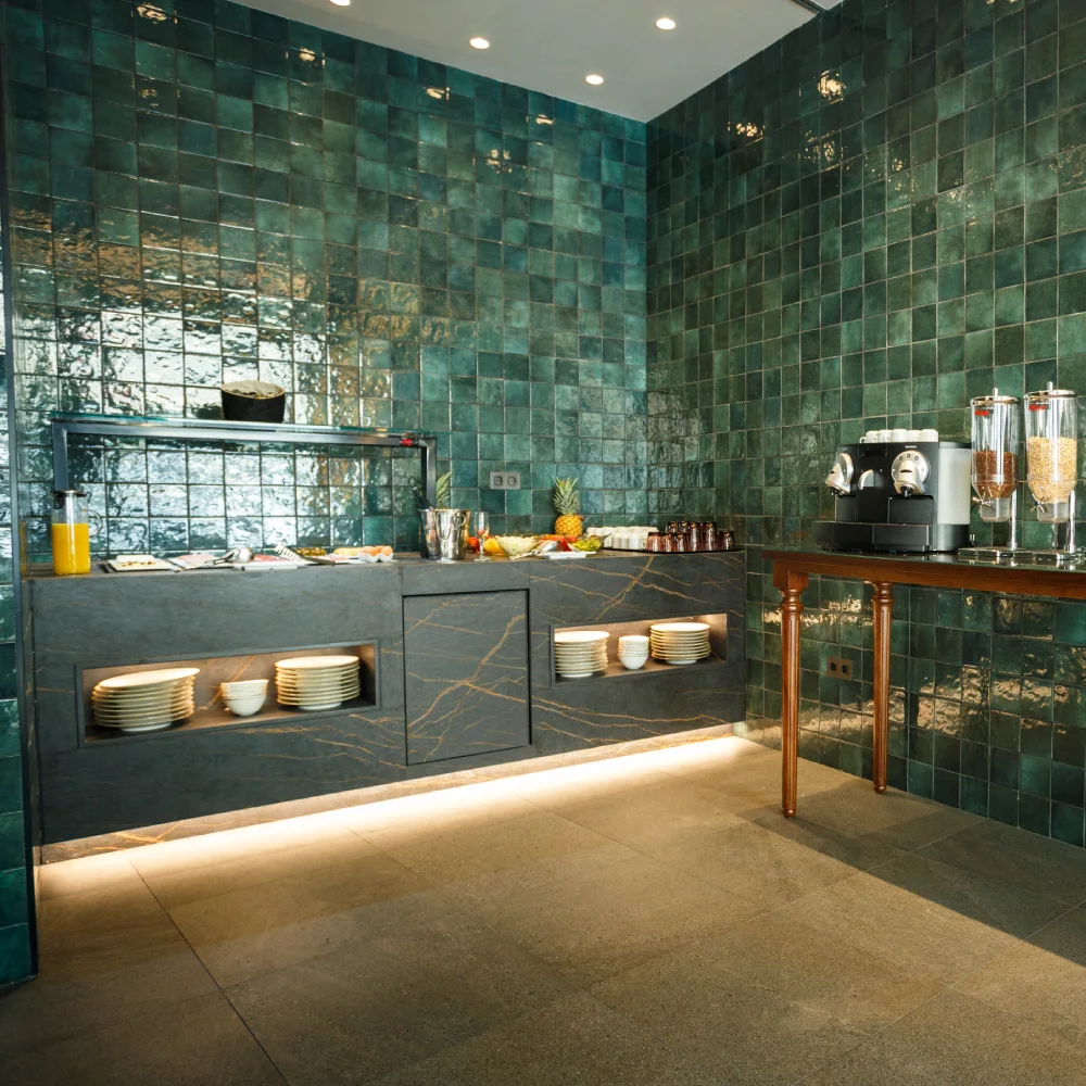 Buffet con azulejos verdes, cafetera y dispensadores de bebidas en una cocina.