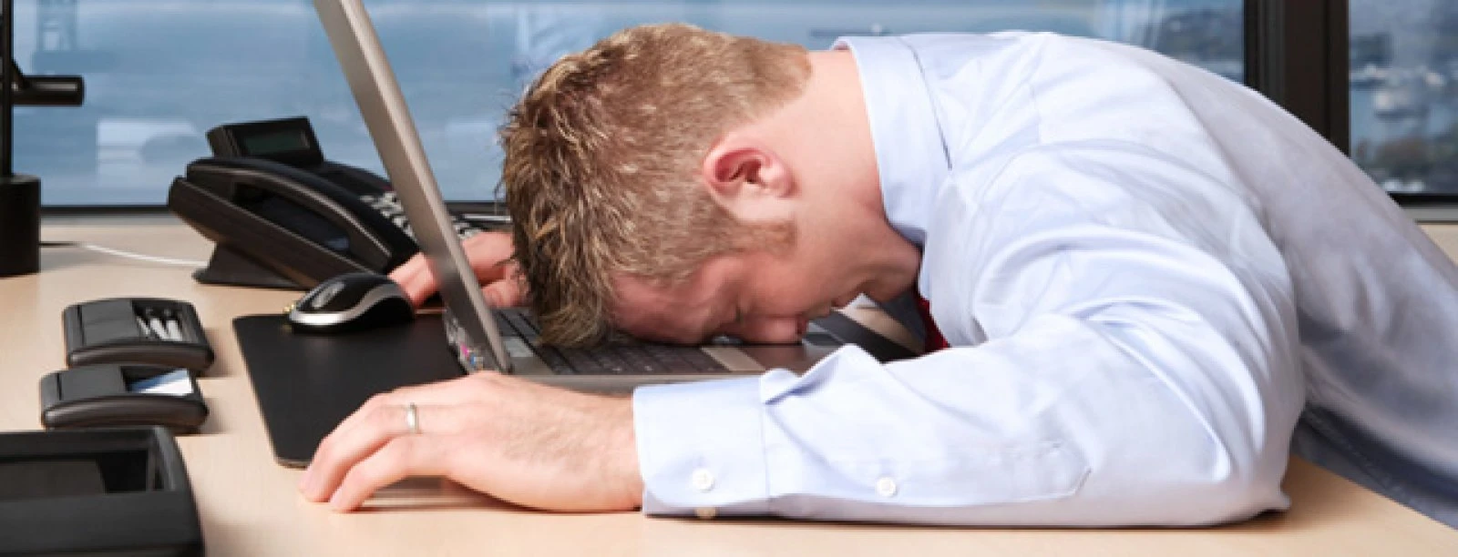 Hombre con camisa blanca duerme recostado en oficina junto a una computadora