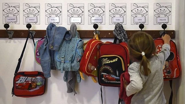 Niños eligiendo mochilas en un expositor; mochilas rojas y azules.
