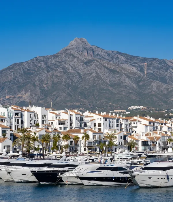 Marina con yates y casas blancas frente a una monta&ntilde;a bajo cielo azul