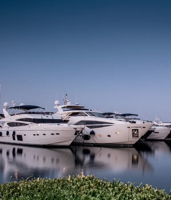 Yates blancos amarrados junto al muelle, reflejados en el agua y cielo azul